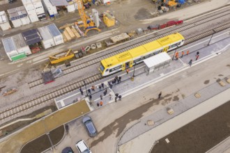 Aerial view of a construction site with a yellow train on tracks and people at the new station