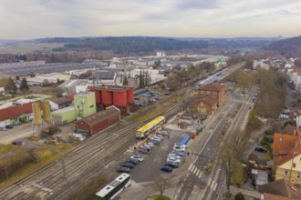 Aerial view of a train station with a yellow train, industrial buildings and parked cars, the