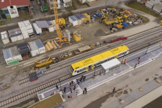 Station scene with yellow train and construction work, workers and cranes against an urban