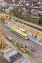 Yellow train under crane on modern construction site, surrounded by urban residential area,