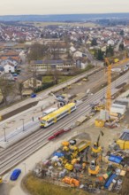 Station under construction with yellow train, construction cranes and houses in the background,