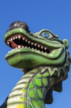 Green dragon with big teeth and long red tongue against blue sky background, Fun Show traveling