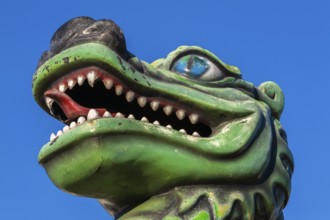 Green dragon with big teeth and long red tongue against blue sky background, Fun Show traveling