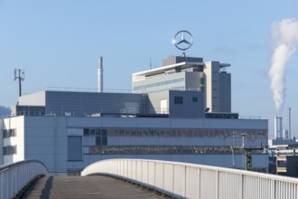 Industrial plant with Mercedes logo on the roof and smoking chimney, crossed by a bridge,