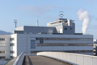 Modern industrial building with Mercedes logo and smoking chimney in the background, blue sky,