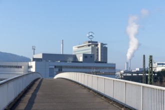 Industrial complex with Mercedes logo and smoking chimney, crossed by bridge, blue sky, Mercedes