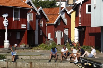 Group of people sitting in front of colorful wooden houses at the harbor, Smögen, Västra Götaland,