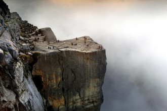 A lonely rock edge emerges from the clouds as the sun illuminates the horizon, Preikestolen,