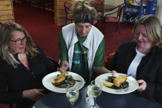 Two woman are served plates of mussels at a restaurant table by a waitress, Havelock Hotel,