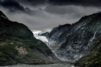 The Franz Josef Glacier with dramatic skies and steep, forested mountain slopes, Franz Josef, West