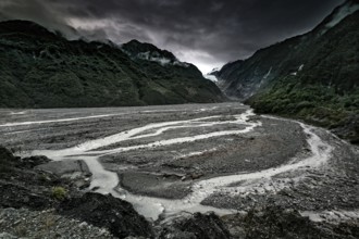 Franz Josef glacier flanked by an extensive riverbed and under dark clouds, Franz Josef, West