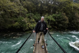 Person standing on a suspension bridge over a fast river, Fjordland National Park, New Zealand