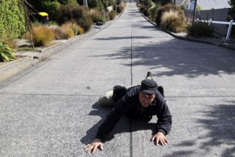 A person humorously lies on steep Baldwin Street in Dunedin, Dunedin, zero, New Zealand
