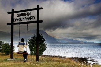 Child swings with a view of Lyngen Fjord under dramatic sky, Lyngen Fjord, Norway