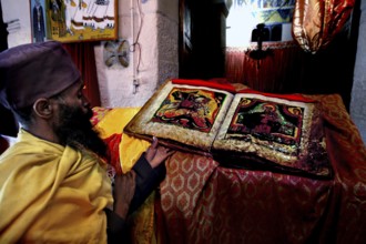 Priest in St. Mary's Cathedral in Axum holding an opened Bible with rich icon images, Axum, Tigray,