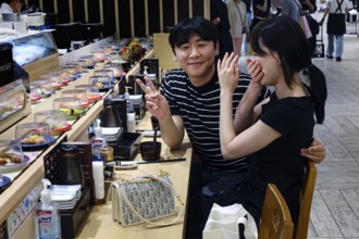 Friends enjoy sushi and laugh at lively restaurant, Busan, South Korea
