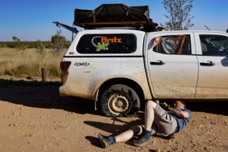 Person repairs flat tire next to a car in Purnululu National Park, Purnululu National Park, Western