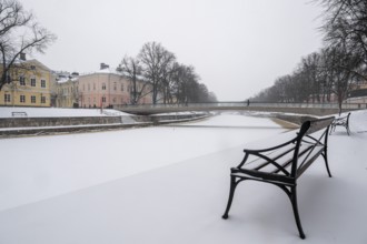Bench, historic buildings on the frozen Aurajoki River, wintery Turku or Swedish Åbo,