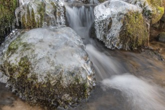 Branches are covered with ice near the river. The water flows gently and forms ice formations on
