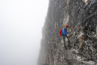 Mountaineers on a steep rock face on the Via Ferrata Oliva Detassis via ferrata in fog, steep