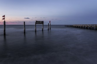 Wooden sign in the sea with inscription Zingst and wooden walkway, long exposure, evening light,