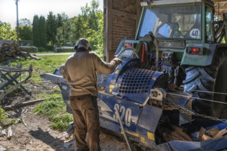 Young man sawing and splitting beech logs with his saw cutting machine, powered by a tractor in a