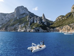 Couple on motorboat off picturesque rocky coast, cliffs with L'Aguglia pinnacle, blue sea and Cala