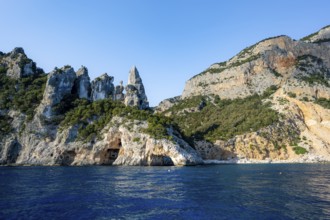 Picturesque rocky coast, cliffs with caves in the morning light, L'Aguglia rock peak, blue sea and