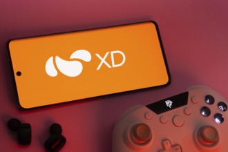 Dhaka, Bangladesh- 22 Mar 2025: Smartphone with XD logo, game controller, and earbuds on a pink