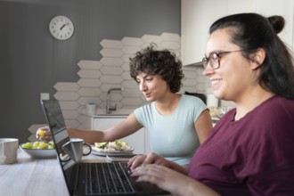 A couple sitting at a kitchen table, enjoying breakfast while working on laptops. They are relaxed