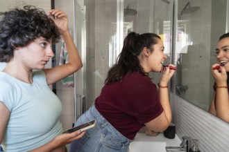 A lesbian couple shares a morning routine in the bathroom, with one applying makeup and the other