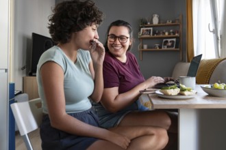 A lesbian couple shares a cozy breakfast in their modern kitchen, with one partner working on a