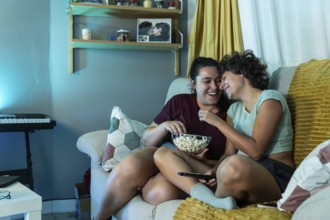 A joyful lesbian couple eating popcorn while watch tv, highlighting domestic harmony and love