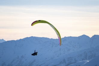 Paragliders flying over snowy mountain peaks in winter in evening light, Kitzbühel Alps, Tyrol,