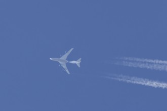 Boeing 747 jumbo jet cargo aircraft flying in a blue sky with contrails or vapour trails behind,