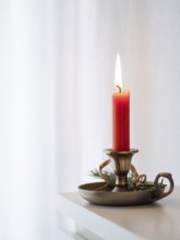 Red candle burning on a brass candlestick decorated with tree branch