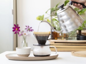 Barista preparing filter coffee using a modern kettle and a ceramic dripper