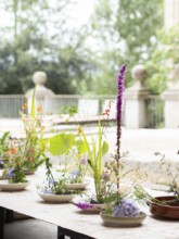 Colorful ikebana flower arrangements sitting in shallow bowls on a table during an outdoor workshop