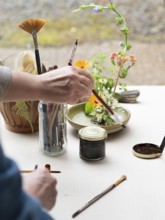 Florist creating ikebana arrangement, painting kenzan and arranging flowers on a table