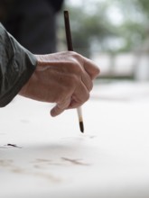 Hand holding a brush and painting on a white canvas during an ikebana workshop, creating floral