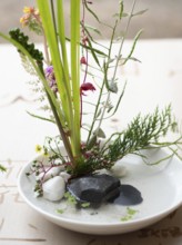 Delicate ikebana flower arrangement in a white bowl with stones and water, showcasing japanese art