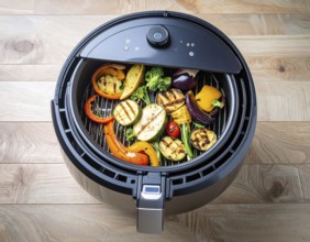 Air fryer with grilled vegetables, wooden table in the kitchen, healthy eating, healthy vegetarian
