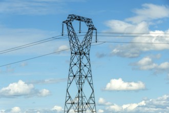 High voltage power lines against a bright blue sky with scattered clouds, Puy de Dome, Auvergne