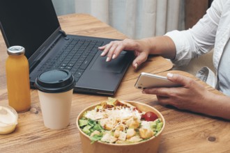 A woman is working on a laptop at home, there is food on the table, salad, coffee and juice,