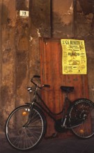 A bike stands in front of an old house wall with a soccer poster of GS Busseto, in honor of