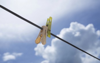 Clothespins on a wire set against a bright blue sky with fluffy clouds