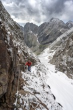 Mountaineer on a rope-secured path in a steep rocky mountain landscape with fresh snow in summer,