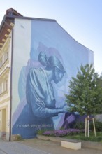 Mural Knowledge by Sokar Uno 2023, blue house wall, woman reading a book, learning, scrolling,