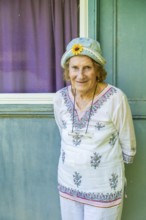 Portrait of a cheerful senior woman wearing a denim hat with a decorative sunflower, standing in