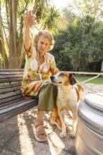 Elderly woman sitting on a wooden bench in a garden, enjoying the company of her loyal dog by her